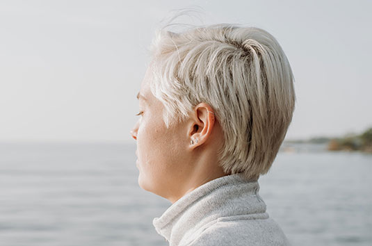 Femme sereine sur le bord de l'eau, visage vers le soleil matinal